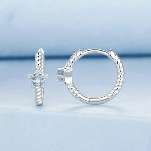 Silver hoop earrings with blue gemstones on a light blue background