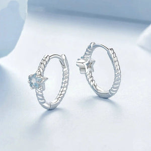 Pair of silver hoop earrings with star and flower designs on a light blue background