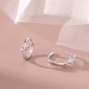 Silver open earrings with star designs on a soft pink background