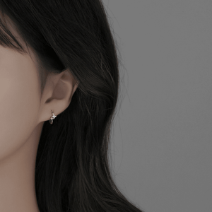 Close-up of an ear wearing a small earring with dark hair and a neutral background