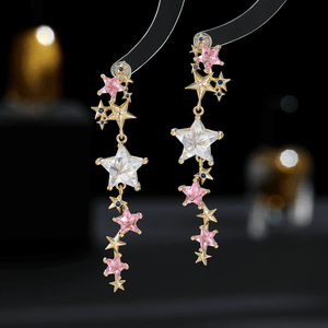 Star-shaped earrings with pink and clear stones on a dark background