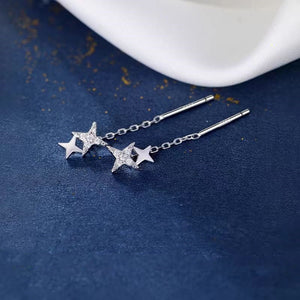 Silver star-shaped earrings on a blue surface with a white dish in the background