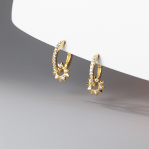 Gold hoop earrings with star-like designs on a gray surface