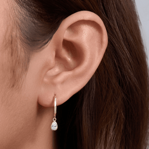 Close-up of an ear wearing a gold hoop earring with a teardrop-shaped gemstone.