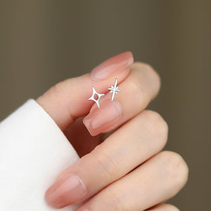 Silver star-shaped earrings held between fingers against a neutral background