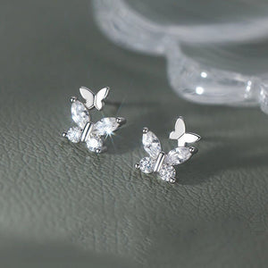 Butterfly-shaped earrings with clear gemstones on a gray surface