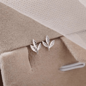 Silver leaf earrings on a soft beige fabric background