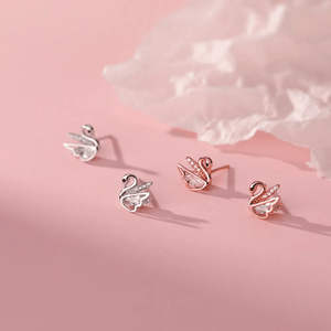 Set of swan-shaped earrings in silver and rose gold on a pink background