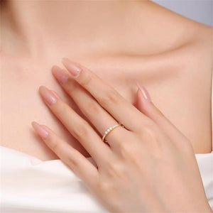A hand displaying three dainty rings, with the top ring featuring a series of small opal stones, the middle ring with a single opal stone, and the bottom ring with a band of cubic zirconia.
