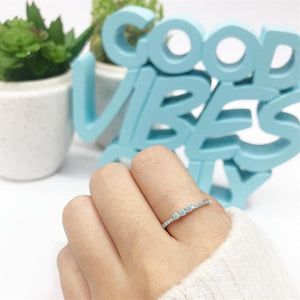 A hand displaying three dainty rings, with the top ring featuring a series of small opal stones, the middle ring with a single opal stone, and the bottom ring with a band of cubic zirconia.
