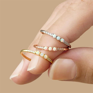 Two opal rings on a finger against a beige background