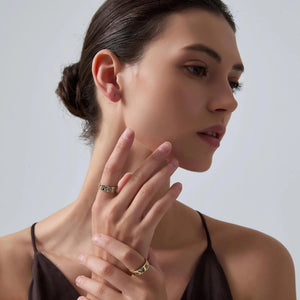 Woman wearing gold rings on her fingers against a plain background