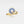 Gold ring with a blue flower-shaped design and pearl center on a white background