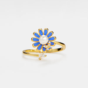 Gold ring with a blue flower-shaped design and pearl center on a white background