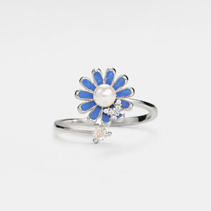 A gold-colored fidget spinner ring with a daisy flower design, featuring blue enamel petals and a pearl-like center, adorned with small cubic zirconia crystals.