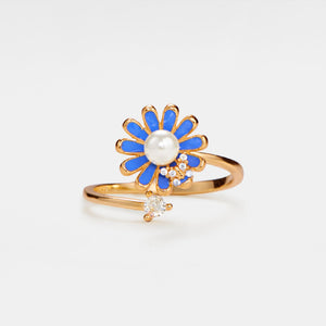 A gold-colored fidget spinner ring with a daisy flower design, featuring blue enamel petals and a pearl-like center, adorned with small cubic zirconia crystals.