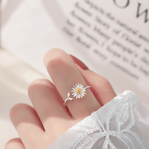 Silver ring with a daisy design on a finger against a blurred background