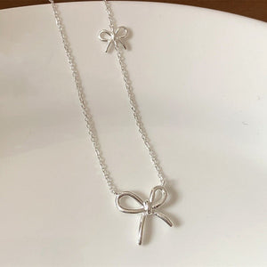 Silver bow-shaped necklace on a white surface