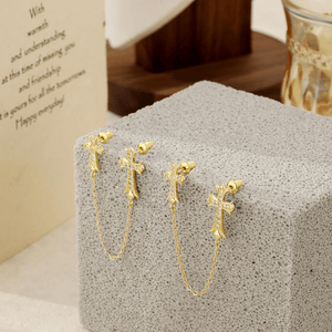 Gold cross earrings on a textured gray surface with a card in the background.