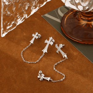 Silver cross-shaped earrings on a brown surface with a glass of red wine in the background.