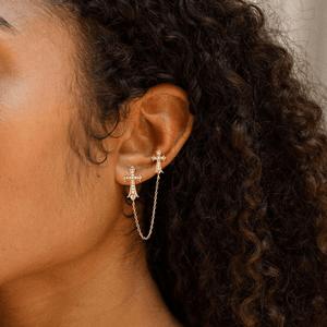 Close-up of an ear wearing a gold cross earring with a chain.