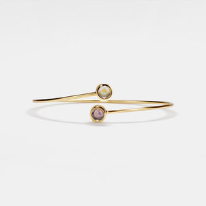 Gold bracelet with two round gemstones on a light gray background