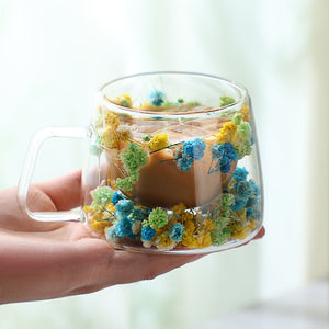 Clear mug with floral decorations held by a hand against a blurred background