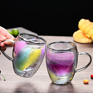 Two glass mugs with colorful feather decorations on a wooden surface.