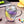 Two glass coffee cups with double wall and feather patterns, one cup is being filled with a liquid while the other remains empty, placed on a table with decorative items around.