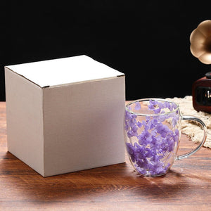 Two clear glass coffee cups with purple and blue flower petals embedded within, placed on a wooden tray.
