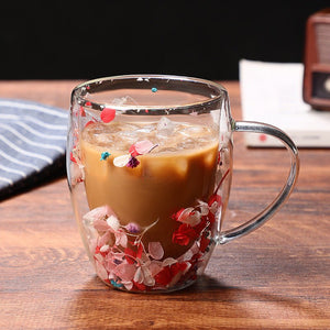 A glass coffee cup with a floral pattern, specifically red and pink flowers, with a creamer or milk substitute visible inside the cup.