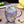 Two glass coffee cups with floral patterns, one held in each hand. One cup has a pink floral design, and the other has a green and purple floral design.