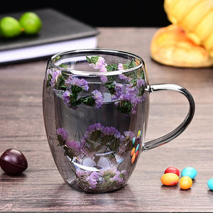 Two glass coffee cups with floral patterns, one held in each hand. One cup has a pink floral design, and the other has a green and purple floral design.