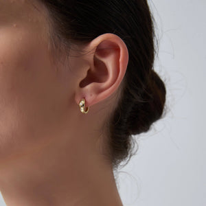 Close-up of an ear wearing a gold hoop earring with a neutral background