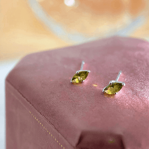 Green gemstone stud earrings on a pink jewelry box with a blurred background