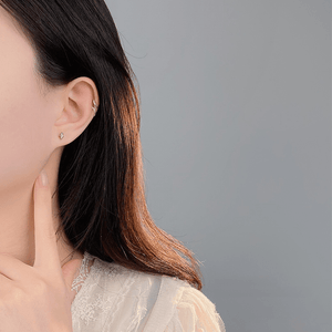 Close-up of a person wearing a gold earring on a gray background