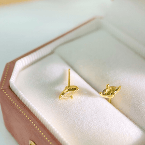 Gold earrings with green gemstones on a pink jewelry box