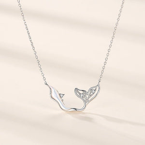 Silver necklace with a whale tail pendant on a beige background