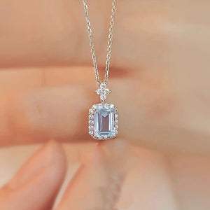 Silver necklace with a pendant featuring a blue gemstone held by a hand against a blurred background.