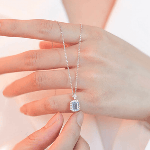 Silver necklace with a pendant held by a hand against a light background