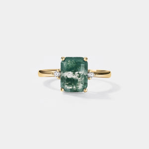 Gold ring with a green gemstone and small diamonds on a light gray background