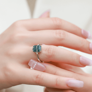 Close-up of a hand wearing a ring with a green gemstone on a blurred background