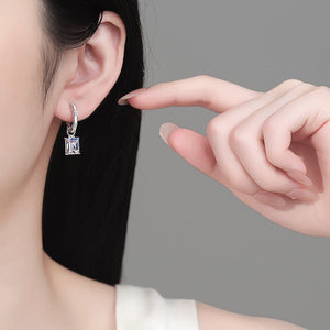 Person wearing a silver earring with a hand pointing to it against a gray background