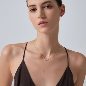 Woman wearing a delicate gold necklace against a plain background