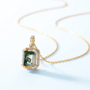 An emerald cut moss agate pendant necklace with gold plating and a chain, showcasing a central green stone surrounded by smaller clear stones.