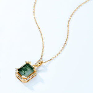 Gold necklace with a green gemstone pendant on a white background