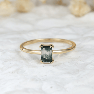 Gold ring with a green gemstone on a white marble surface