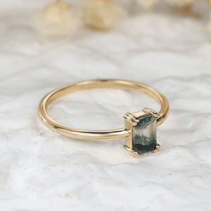 Gold ring with a green gemstone on a marble surface