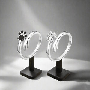 Two silver paw-shaped rings on black stands against a gray background