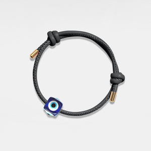 Black cord bracelet with a blue evil eye charm on a light gray background
